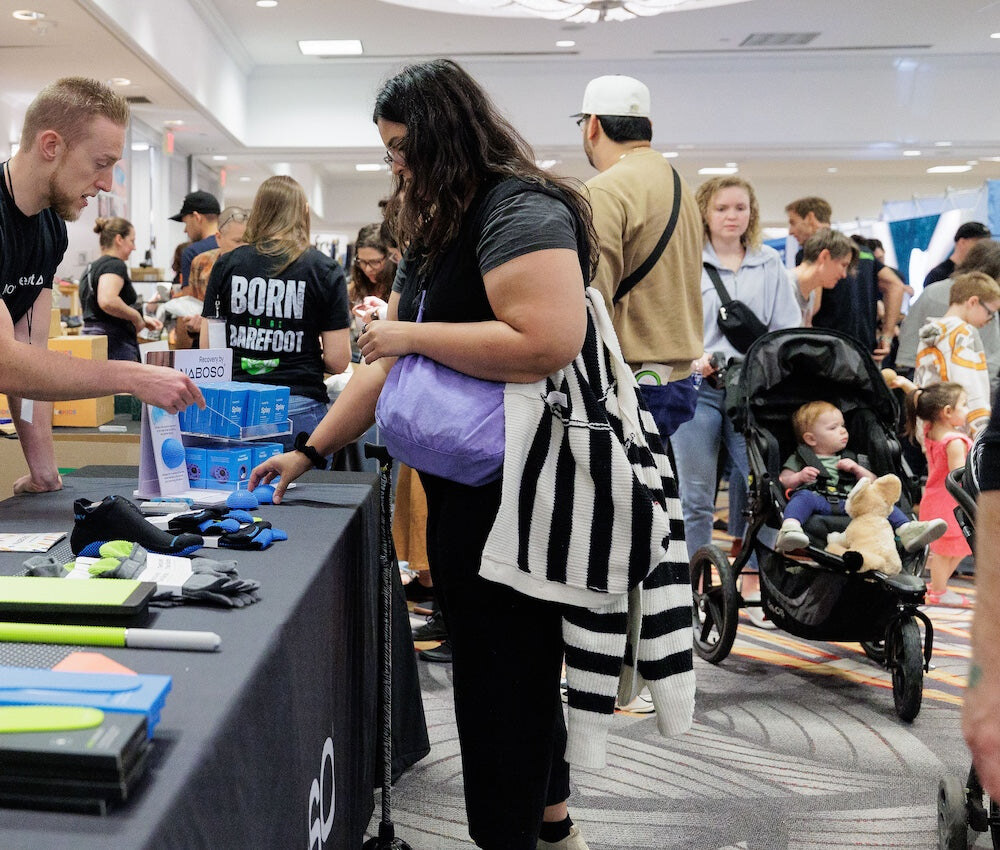 A visitor discussing footwear with an exhibitor in the busy hall, photo by Barefoot Shoe Expo
