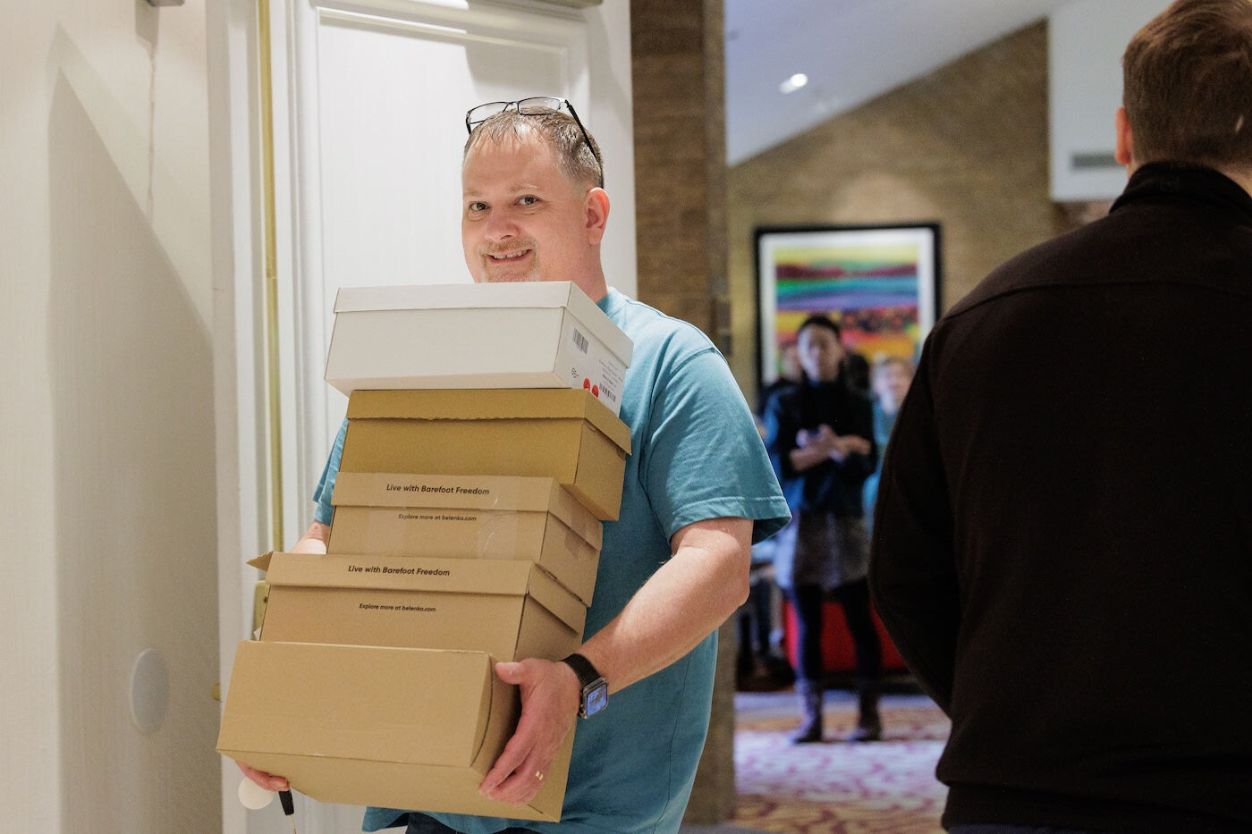 A visitor carrying a stack of shoe boxes through the expo, photo by Barefoot Shoe Expo